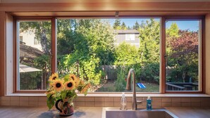 Una cucina con una grande finestra, un lavandino in acciaio inossidabile e un vaso con girasoli.