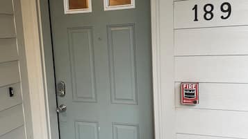 A light gray front door with a keypad lock, a fire alarm, and a mailbox.