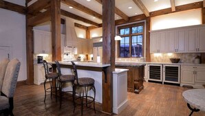 A spacious kitchen with wooden beams, white cabinets, and a large island with bar stools. - Timberhaven (Crested Butte)