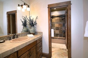 Un baño con un lavamanos color beige, armarios de madera, un espejo con iluminación y una ducha con pared de azulejos.
