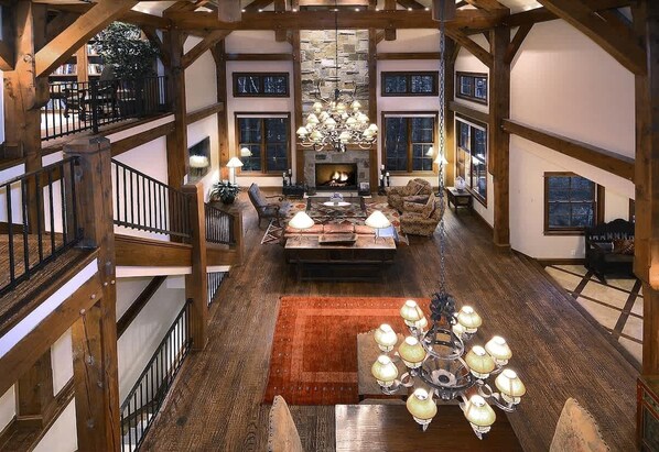 A multi-level interior with a fireplace, wooden beams, and a chandelier.