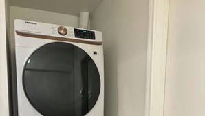 A wall-mounted Samsung washer and dryer unit in a corner, with a door knob visible to the right.