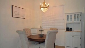 A dining area with a round table, four chairs, a chandelier, a framed certificate on the wall, and a white cabinet with glass doors.