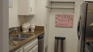 A compact kitchen with a skylight, a stainless steel refrigerator, and a trash can.