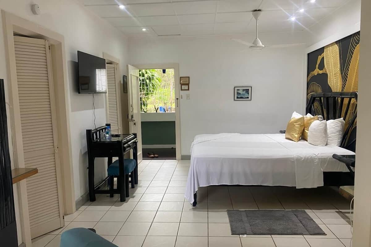 Un dormitorio con cama, escritorio, silla, televisor y puerta que da a un balcón.