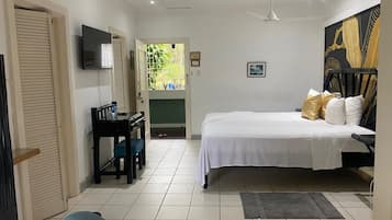 A bedroom with a bed, a desk, a chair, a TV, and a door leading to a balcony.