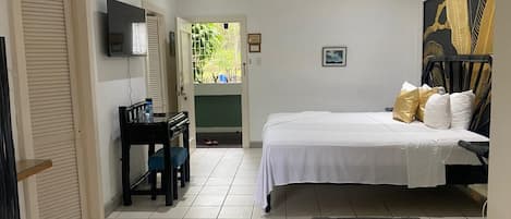 Ein Schlafzimmer mit Bett, Schreibtisch, Stuhl, Fernseher und einer Tür, die auf einen Balkon führt.