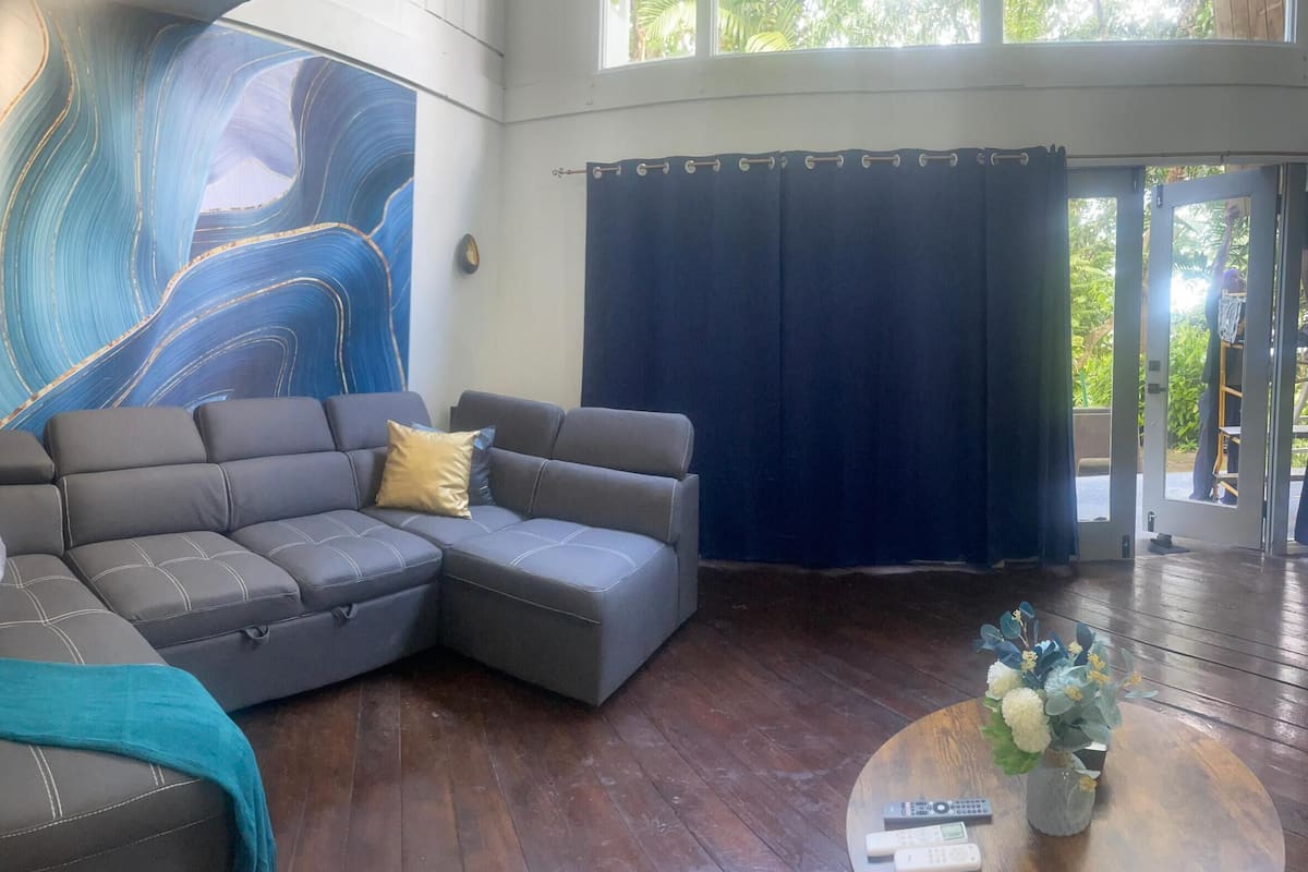 Una sala de estar moderna con un sofá seccional, una mesa de centro con controles remotos y un cuadro abstracto grande en la pared.
