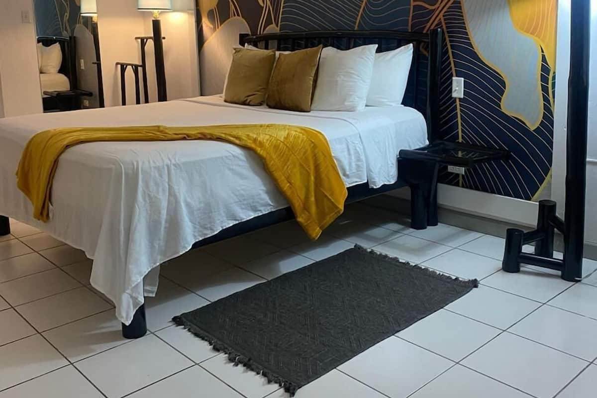 Un dormitorio con cama, un mural grande en la pared, una mesita de noche, una lámpara y una alfombra.