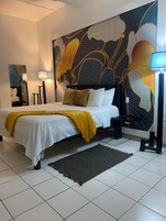 Quarto com cama, um mural grande na parede, mesa de cabeceira, abajur e tapete.