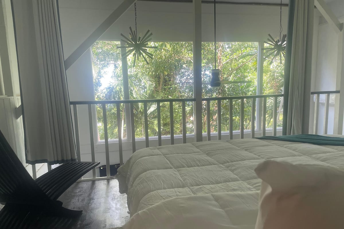 Un dormitorio con cama, una silla, un balcón con barandilla y vistas a zonas verdes.