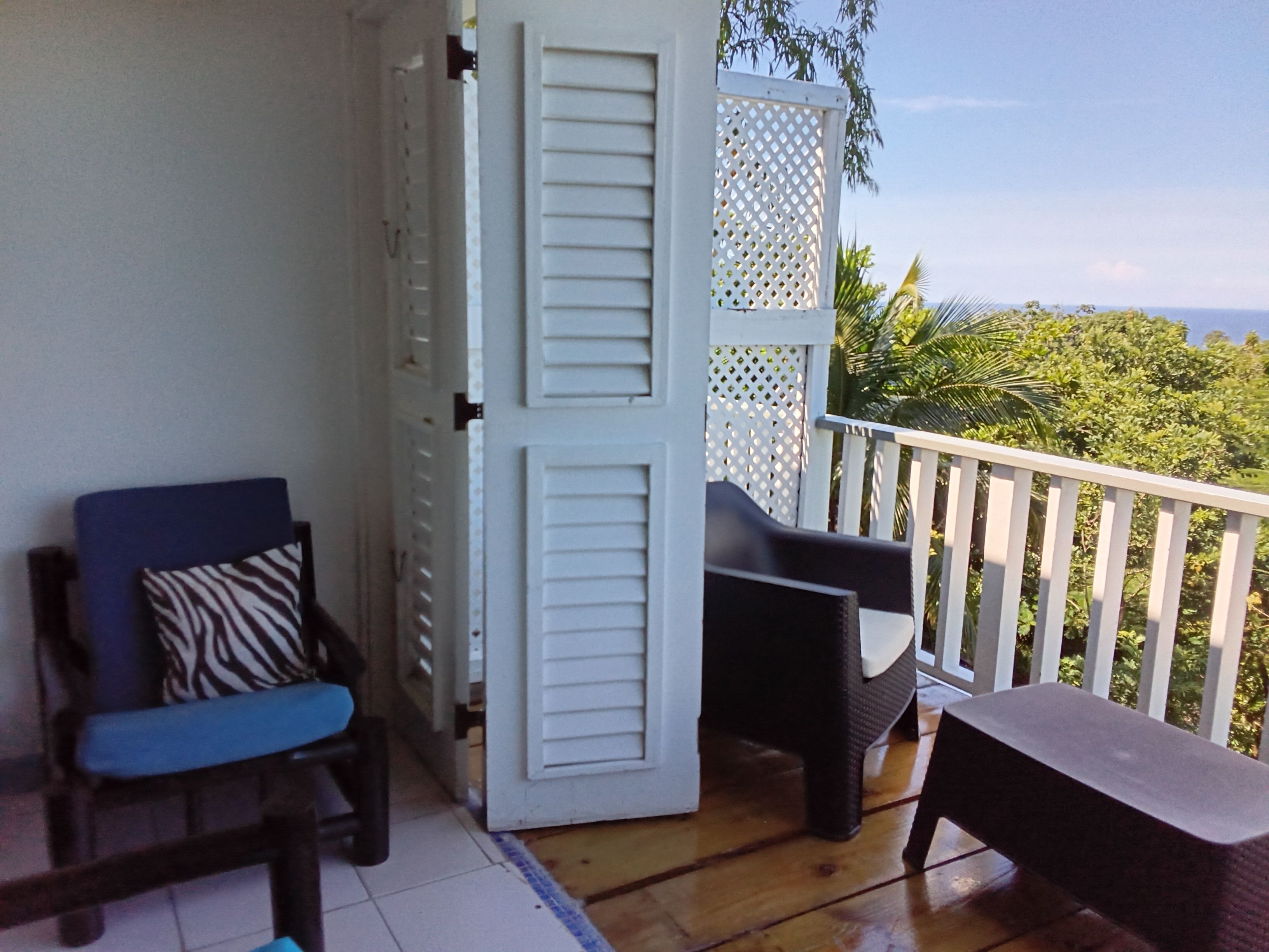 Un balcon avec vue sur l’océan, une chaise avec un coussin à motifs zébrés et une table.