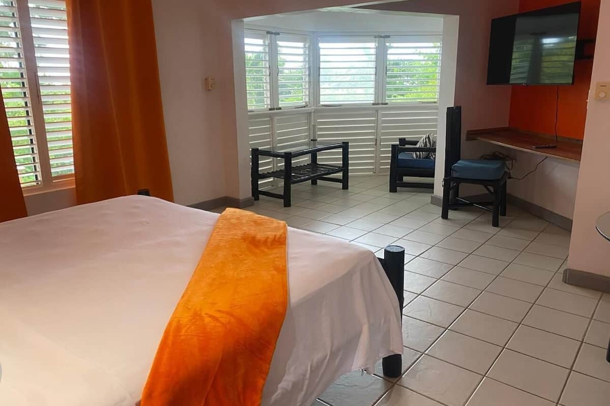Una habitación de hotel con cama, escritorio, silla, televisor y ventana con persianas.