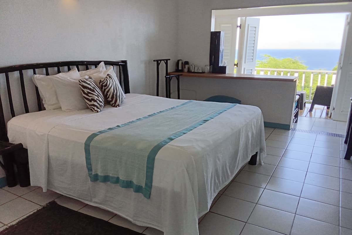 Un dormitorio con cama, almohadas, mesita de noche y vista al océano.