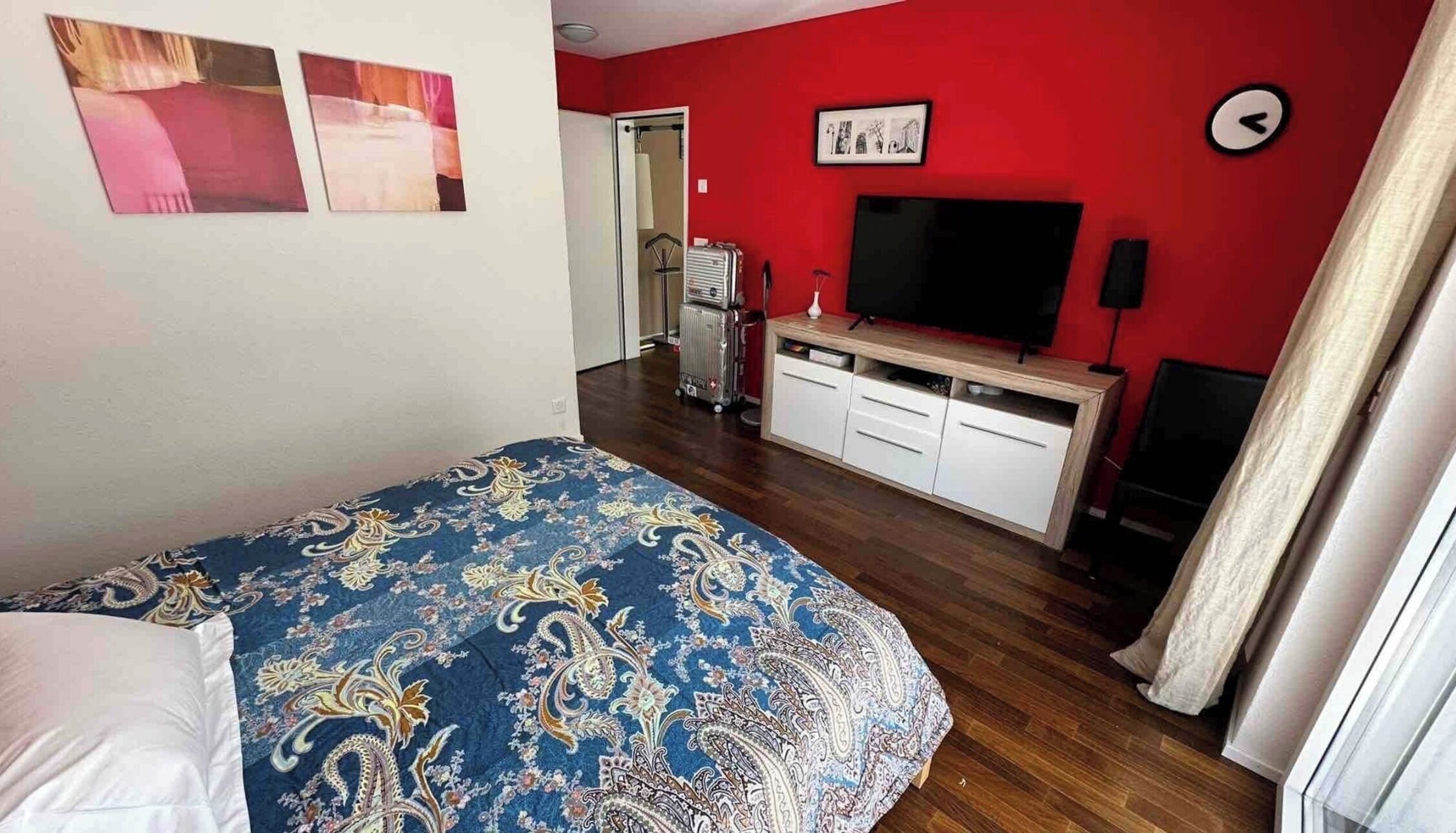 A bedroom with a bed, a TV, a desk, and a suitcase.