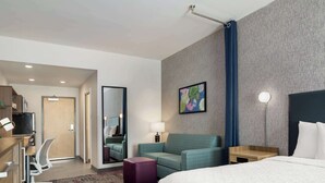 Una habitación de hotel con una cama grande, un escritorio con silla, un sofá, una mesita y un espejo.