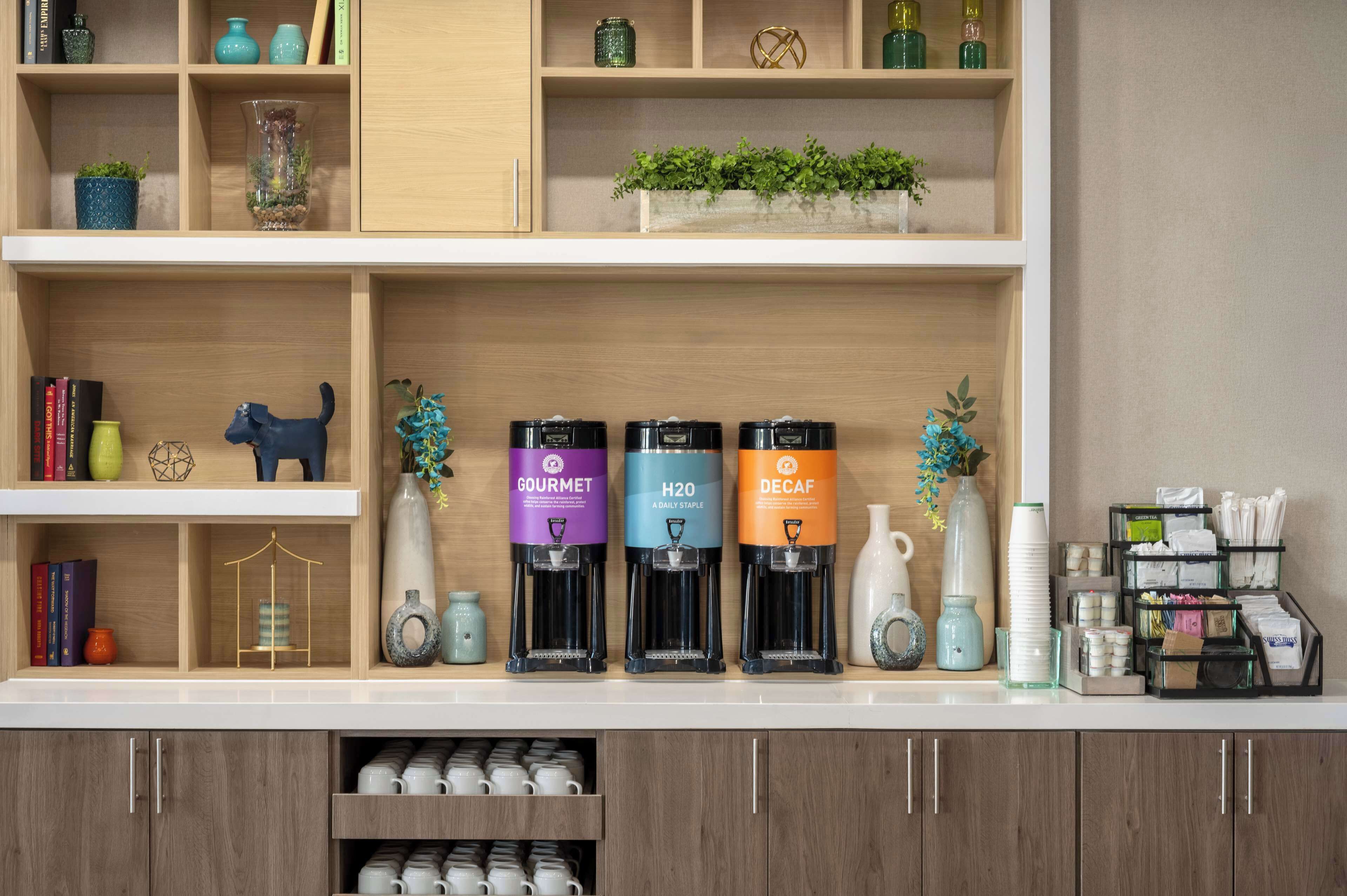 A kitchen counter with a coffee machine, a vase, and a shelf with books and decorative items.