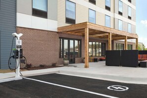 Un edificio moderno con fachada de ladrillo, un espacio cubierto para sentarse al aire libre y un estacionamiento con el símbolo de accesibilidad para sillas de ruedas.