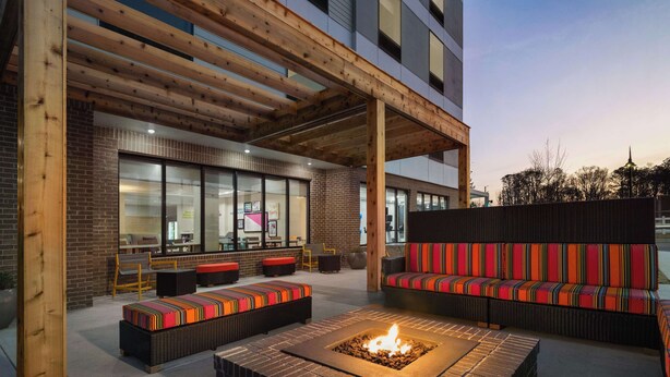 Un área de estar al aire libre con una chimenea, una pérgola de madera y mobiliario moderno.