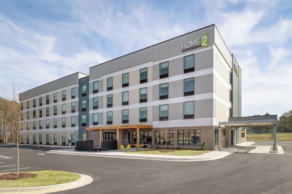 A modern hotel building with a flat facade, multiple windows, and a covered entrance area with outdoor seating. - Home2 Suites By Hilton Conyers Atlanta (Conyers)