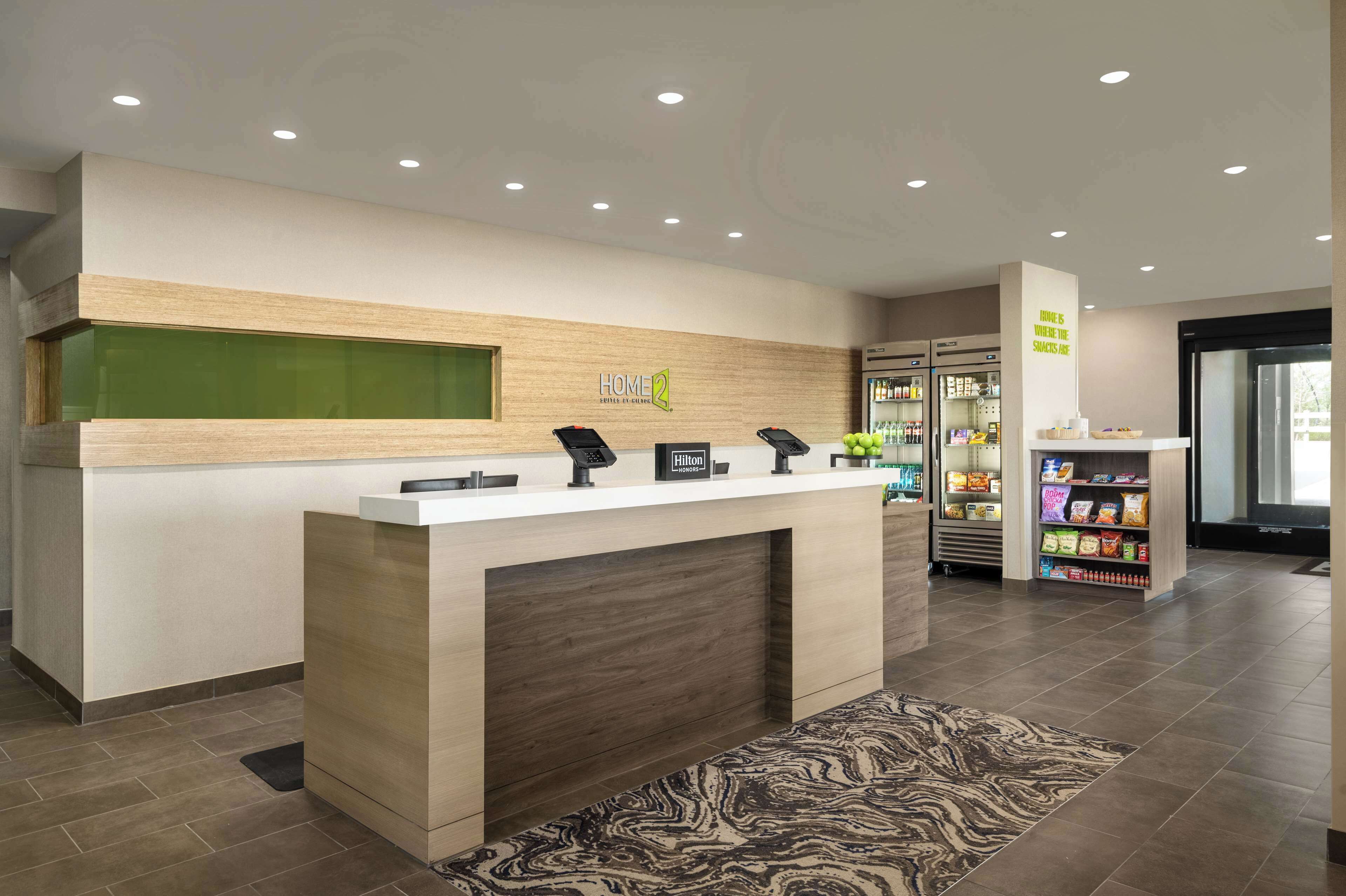 A modern hotel reception desk with a digital kiosk, a minibar, and a snack vending machine.