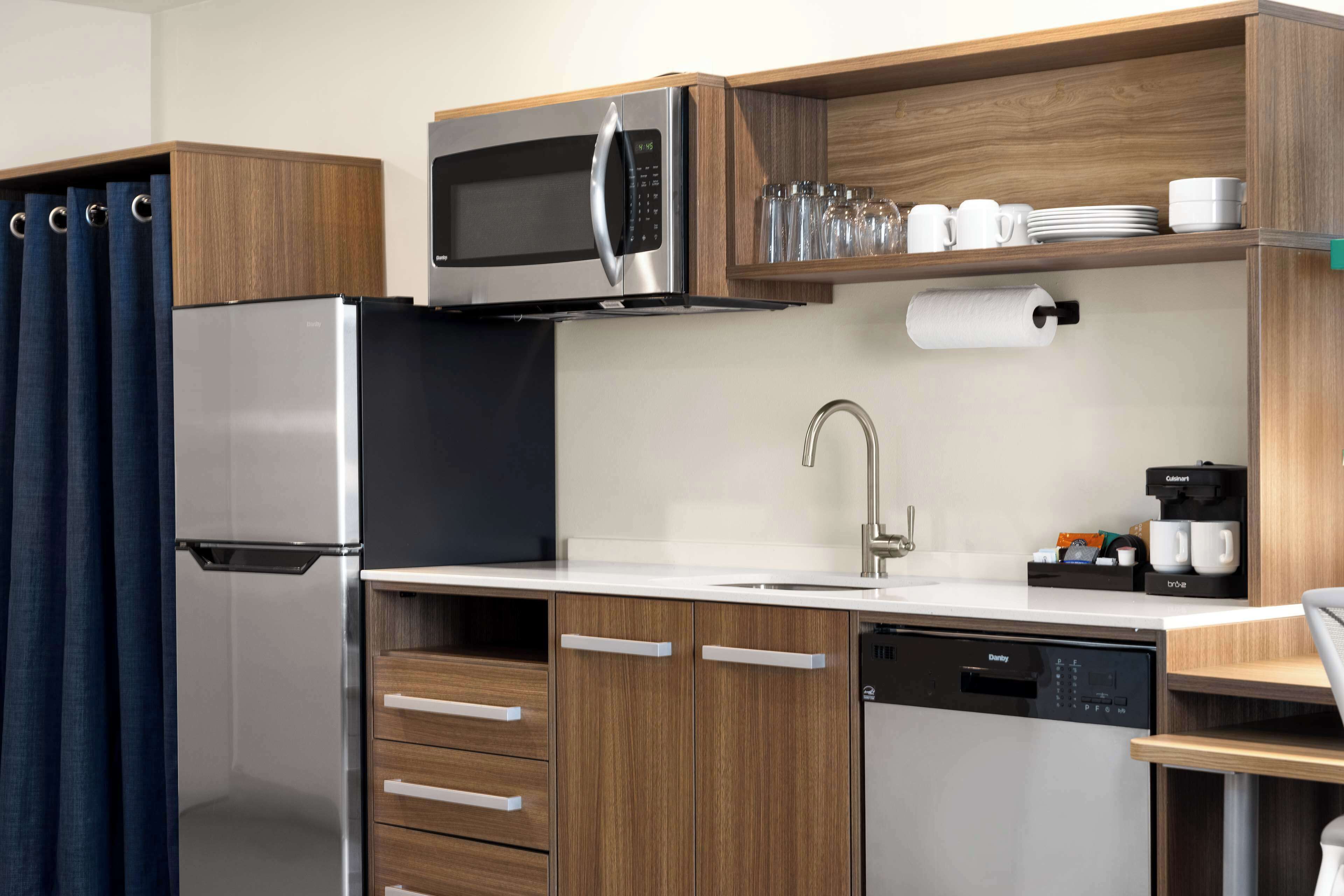 A compact kitchen with a refrigerator, microwave, dishwasher, and wooden cabinets.