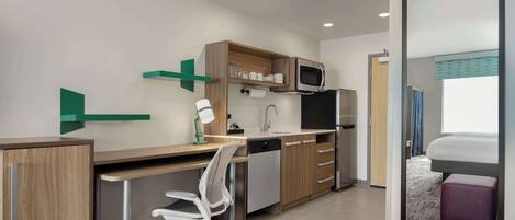 Quarto de hotel compacto com cozinha compacta, uma escrivaninha com cadeira, uma cama e um espelho grande.