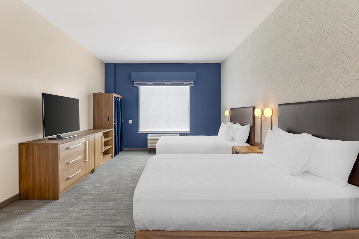 A hotel room with two beds, a TV, a wardrobe, and a window with curtains.