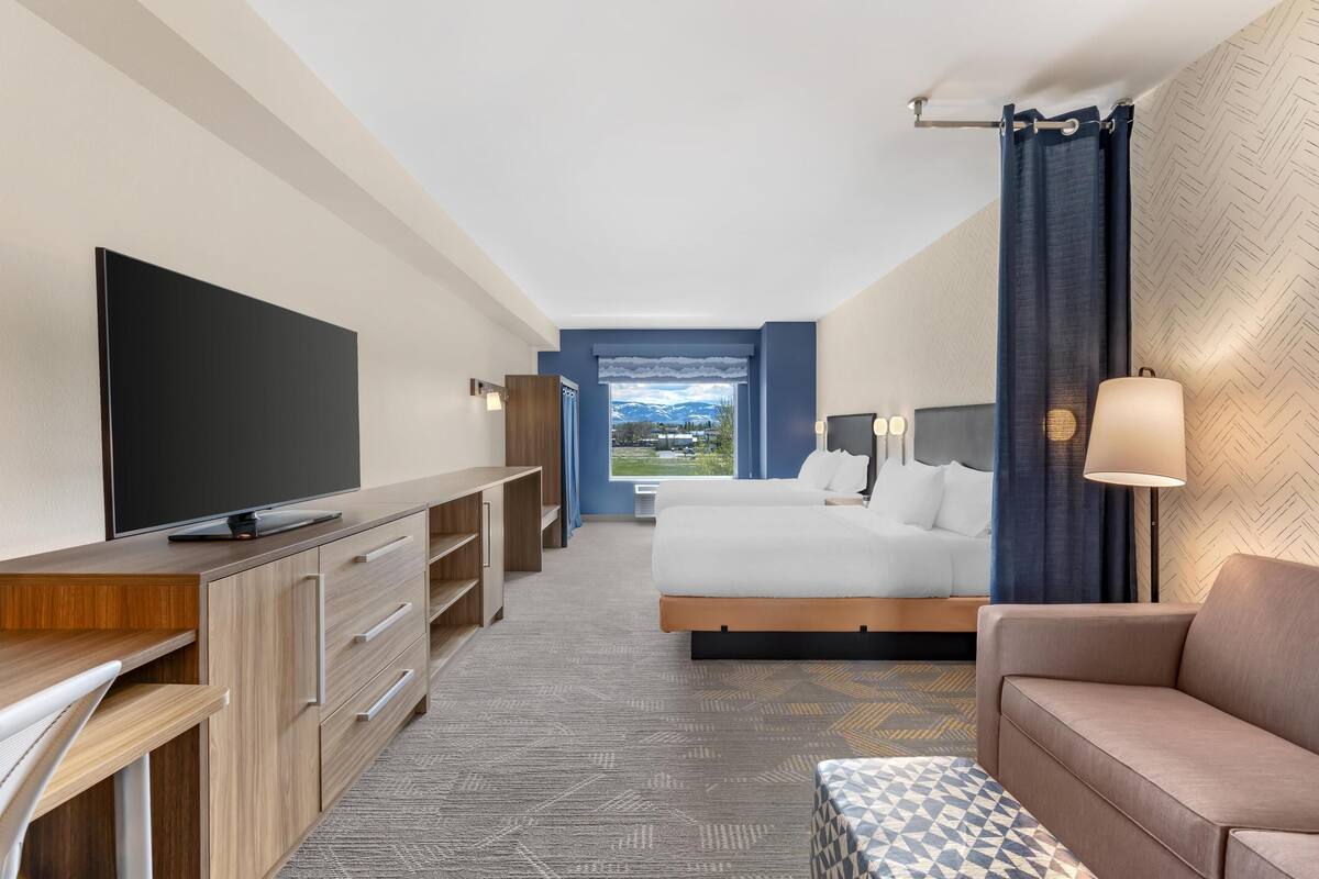 A hotel room with a bed, a TV, a desk, a sofa, and a view of the outdoors.