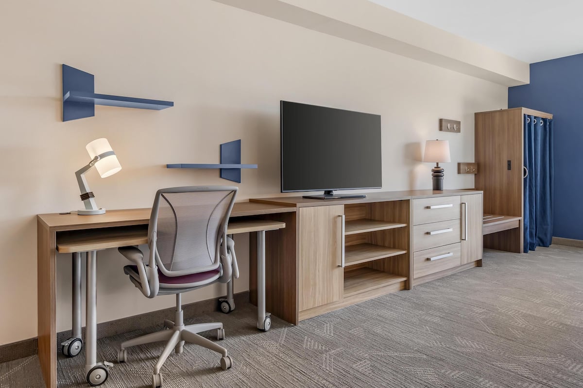 A hotel room with a desk, chair, TV, lamp, and wardrobe.