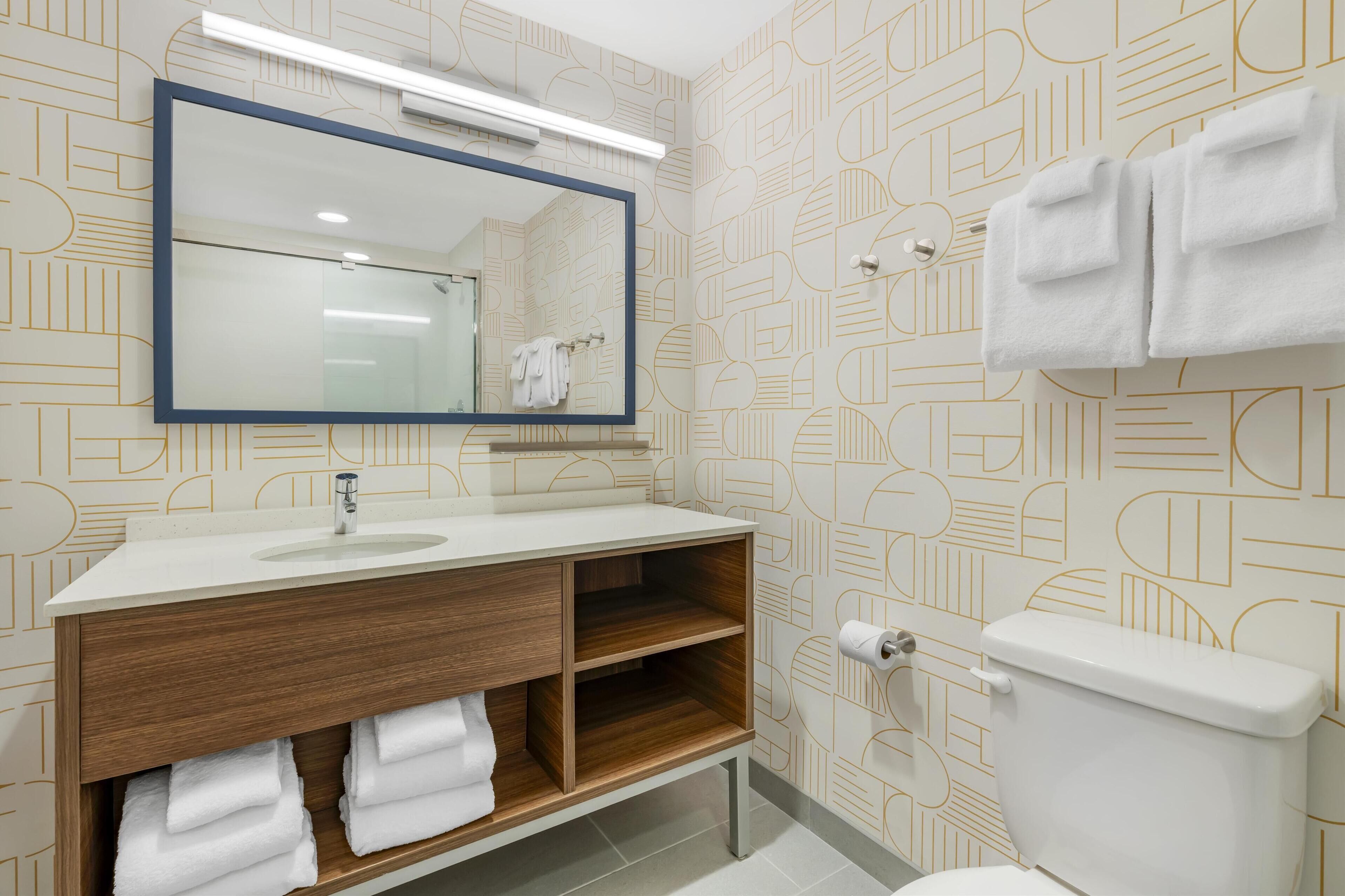 Un baño moderno con un lavamanos blanco, tocador de madera y un inodoro.