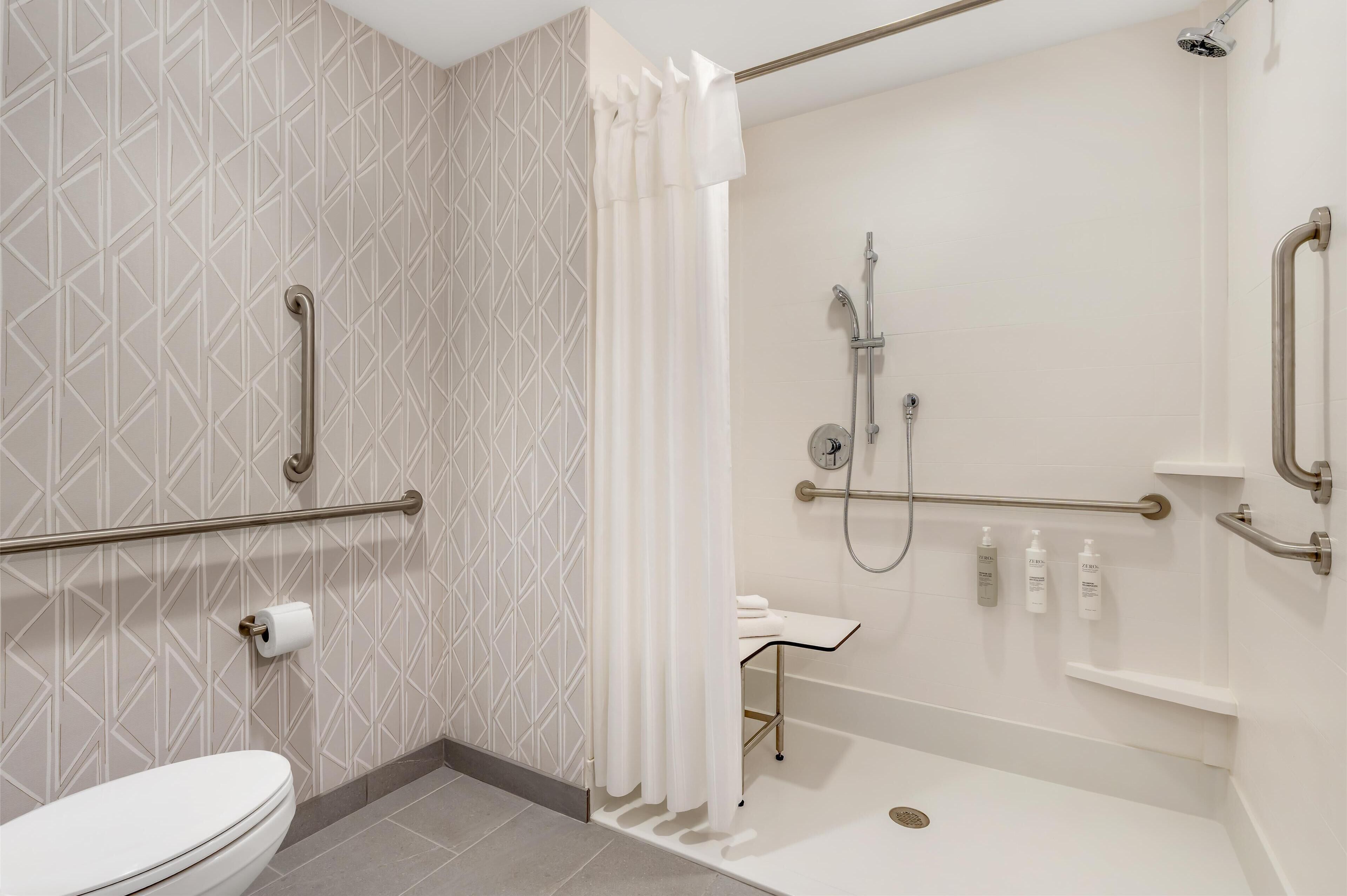 A modern bathroom with a toilet, a shower with grab bars, and a sink with a towel rack.