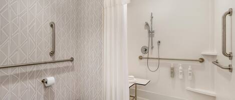 A modern bathroom with a toilet, a shower with grab bars, and a sink with a towel rack.