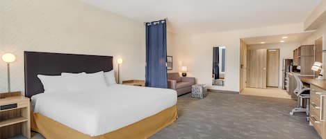 A hotel room with a large bed, a desk, a chair, a sofa, and a bathroom visible through an open door.