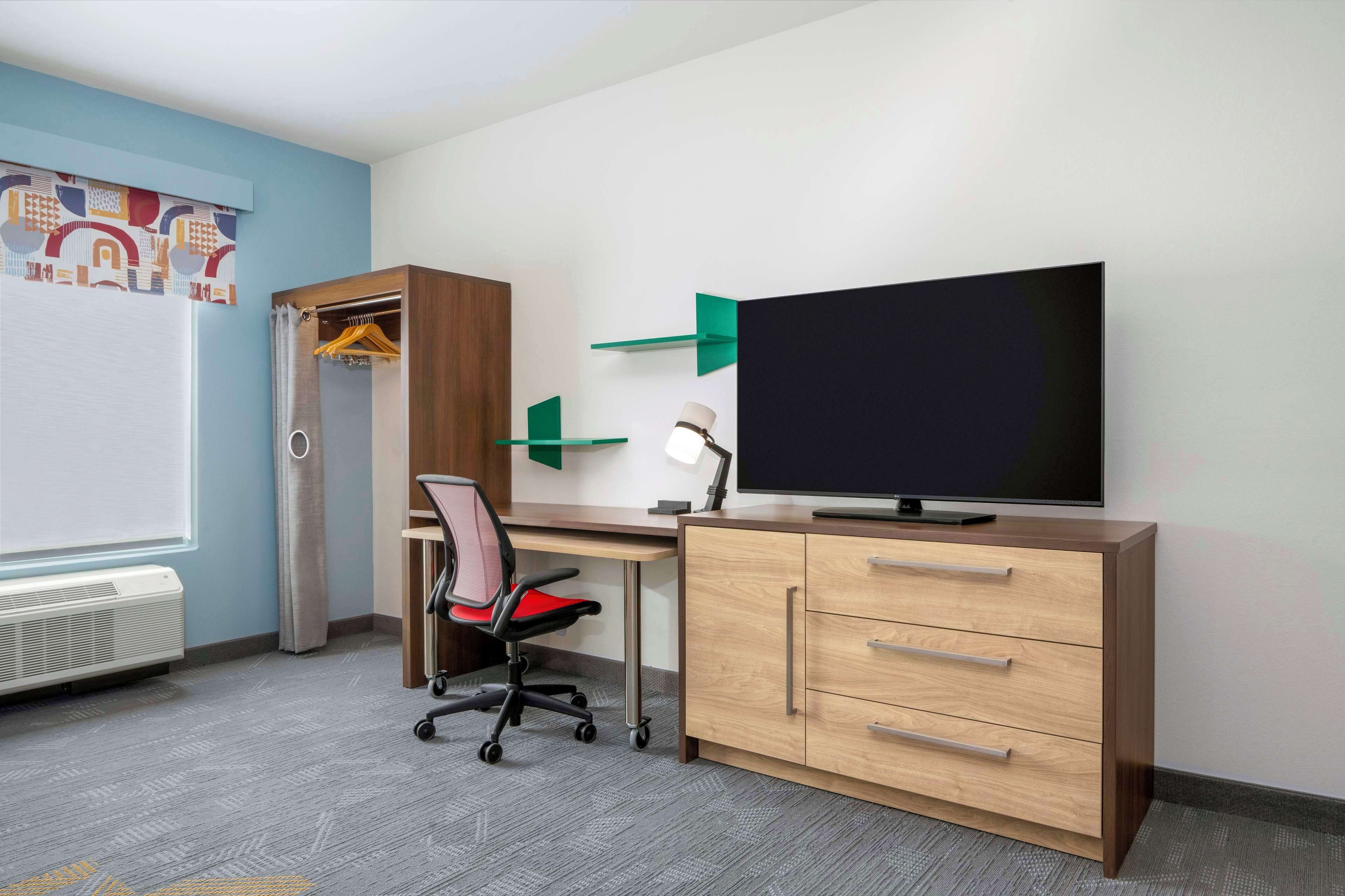 A room with a desk, a chair, a TV, a wardrobe, and a radiator.