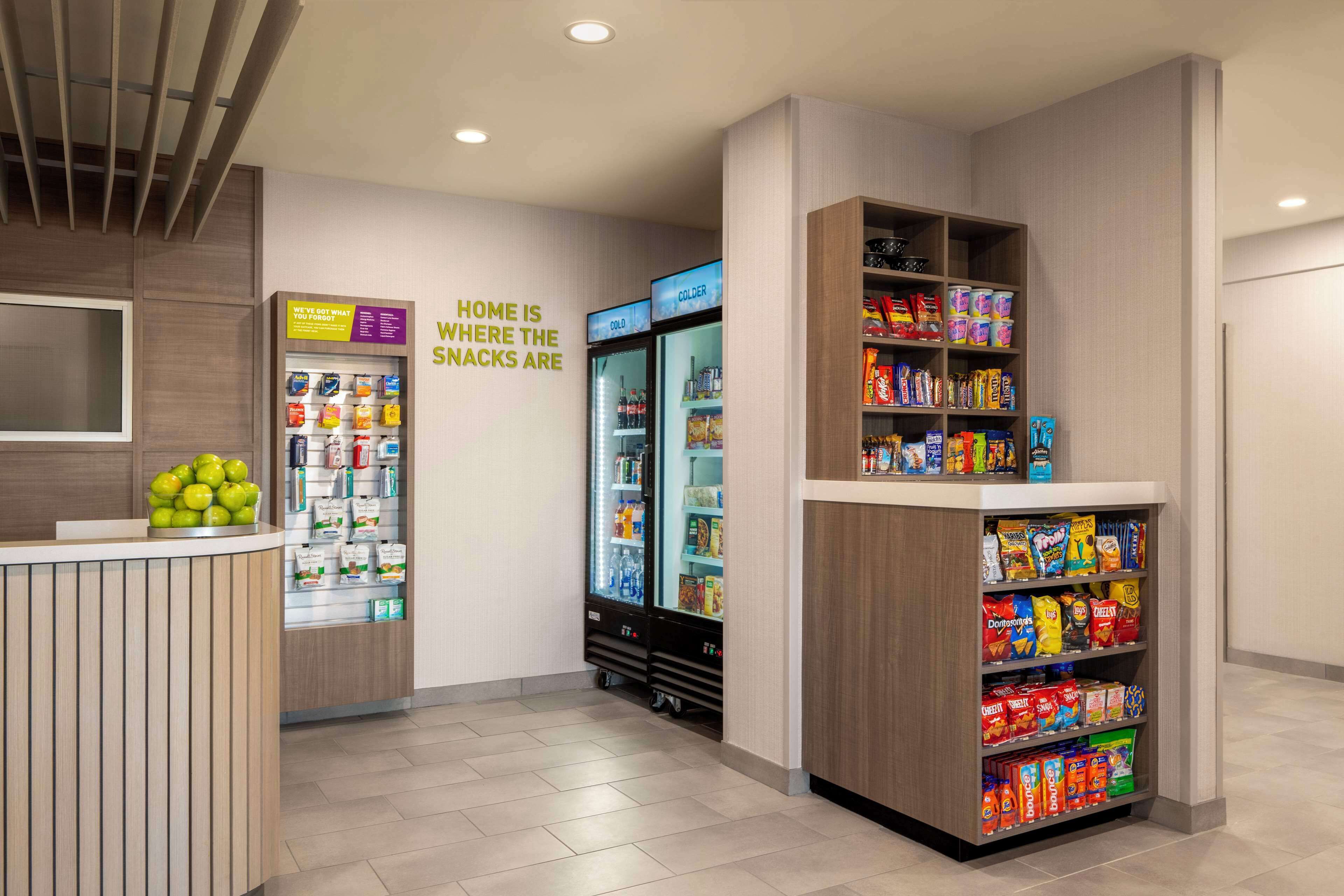 A snack bar with a wooden counter, a refrigerator, and shelves stocked with snacks.