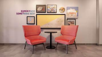 A room with two red chairs and a small round table, a wall with framed artwork, and a sign that reads "WELCOME Jonesboro".