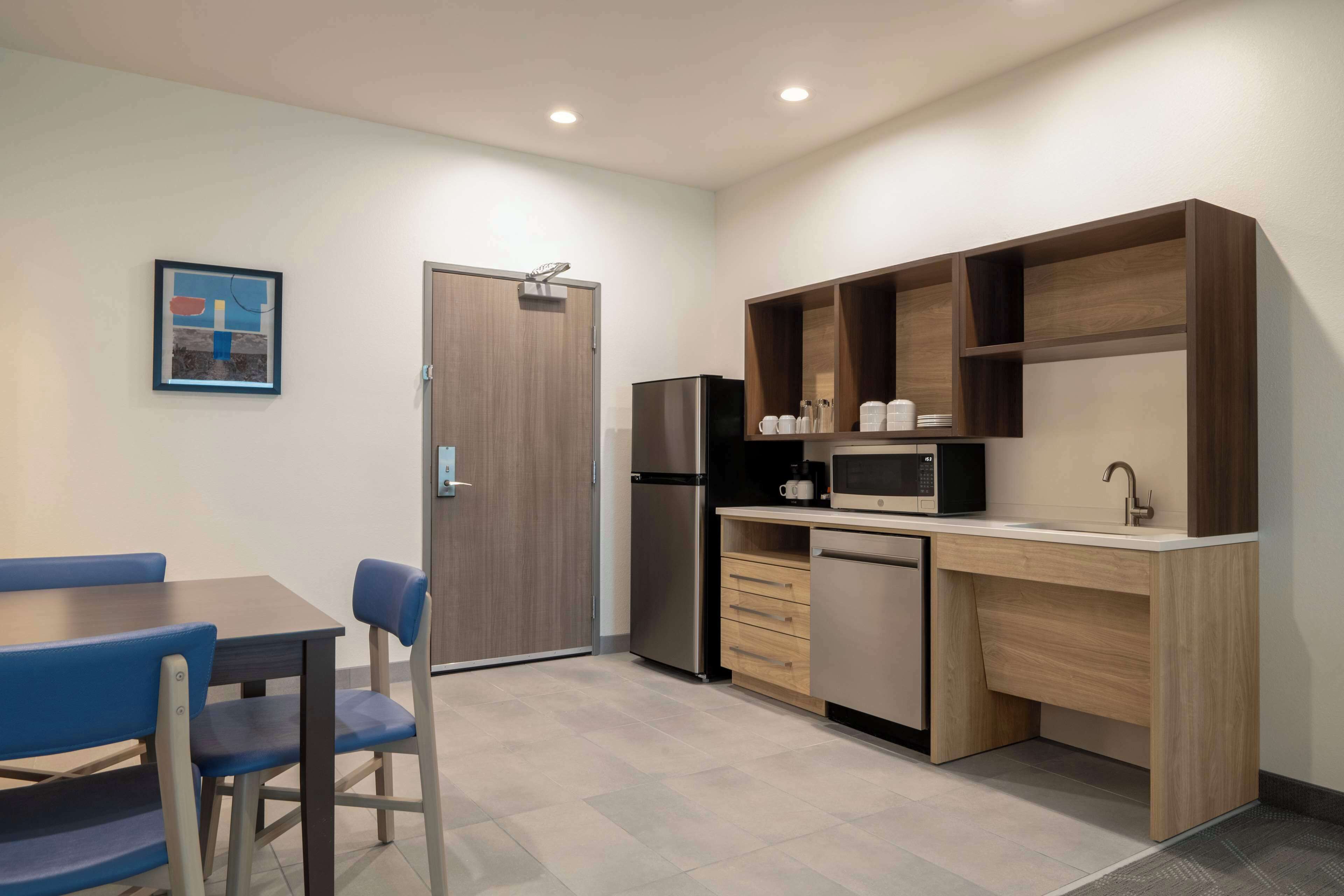 A modern kitchen with a dining table and chairs, a microwave, a refrigerator, and wooden shelves.