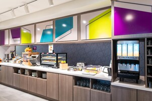 Una barra de desayuno moderna con una máquina de café, una exhibición de frutas y diversas opciones de comida.