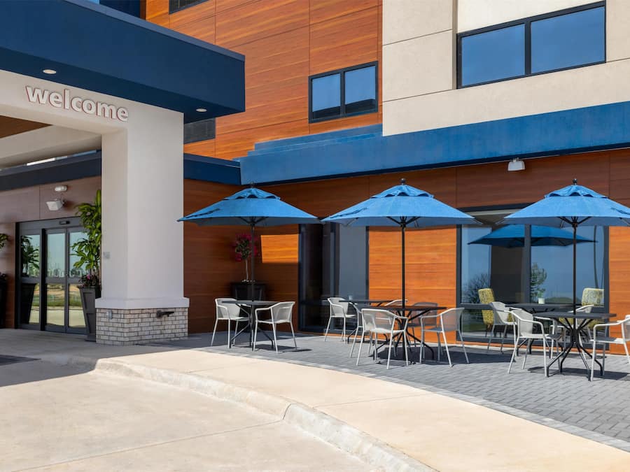 A modern building with a 'welcome' sign, outdoor seating with umbrellas, and a brick pathway.
