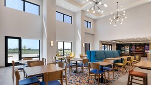 A modern indoor dining area with high ceilings, large windows, and a variety of seating options including tables, chairs, and a blue booth.