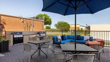 An outdoor patio with a grill, seating area, and umbrella.