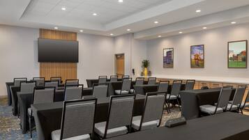 A conference room with rows of tables and chairs, a flat-screen TV, and framed pictures on the wall.