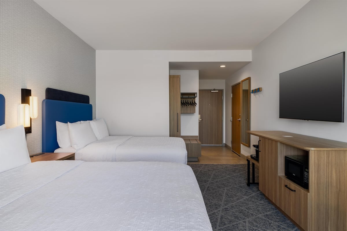 A hotel room with two beds, a TV, a microwave, and a wooden cabinet.