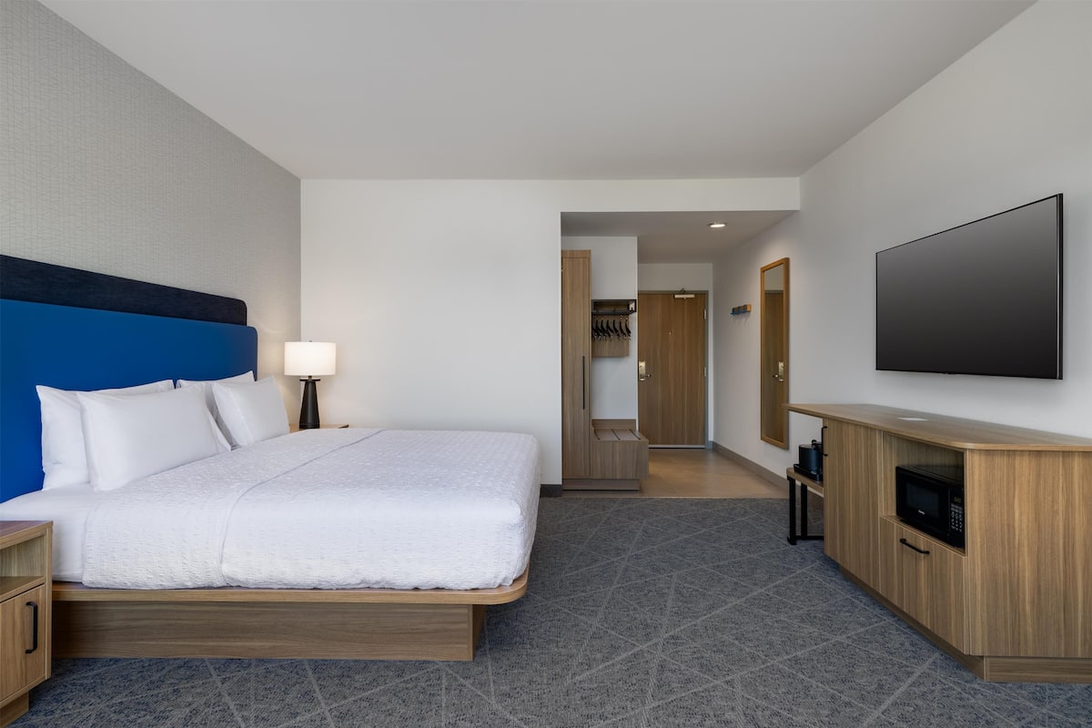 A modern hotel room with a large bed, a TV, a wooden cabinet, and a bathroom visible through an open door.