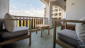 A balcony with a wooden table and two cushioned seating areas, overlooking a building with balconies. - Diani Beachfront Paradise (Diani Beach)