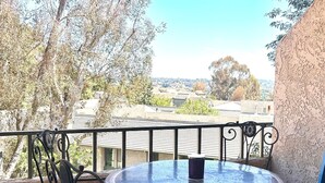 Una mesa redonda con cuatro sillas en un balcón con vistas a árboles y edificios.