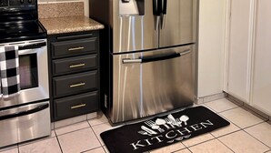 Una cocina con armarios blancos, un refrigerador de acero inoxidable, un microondas y una estufa.