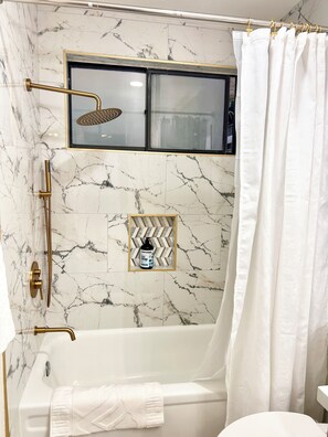 A bathroom with a marble wall, a bathtub, a showerhead, a towel rack, and a shelf with a bottle. - Hillside + View+ First Level + Pool + Remodeled!
Close to USC Keck & Attractions (Los Angeles)