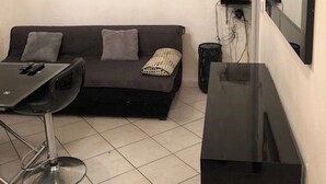 Un espace de vie compact comprenant un canapé, une petite table, une chaise, un téléviseur et un miroir.